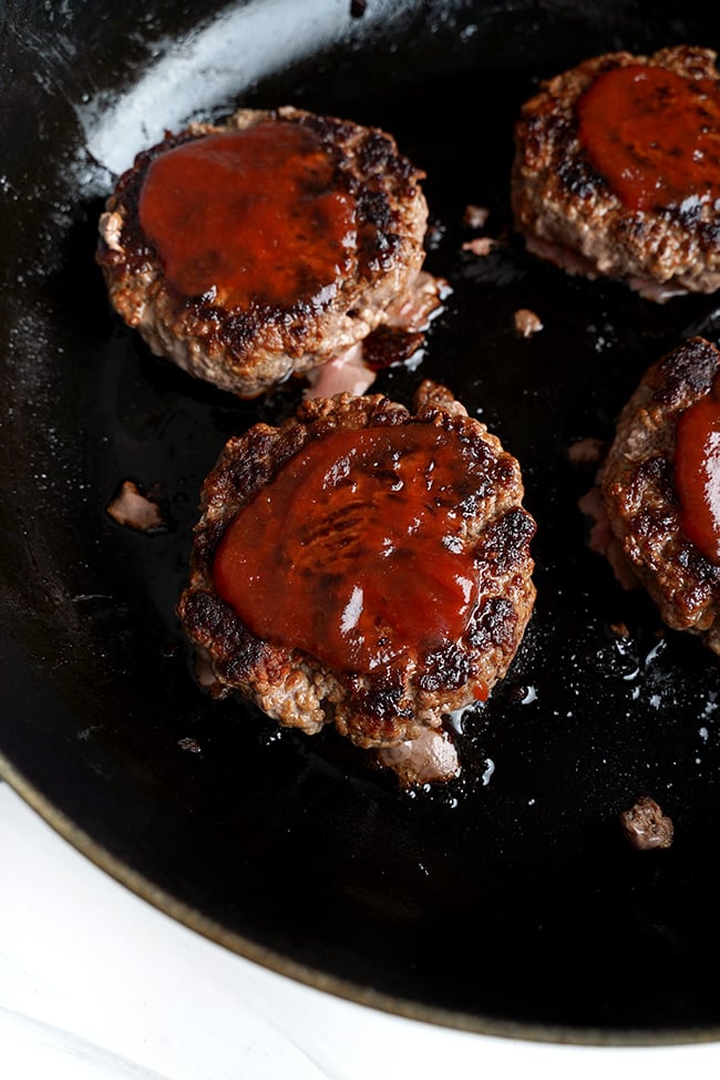 Ketchup wird in einer Pfanne auf Beef-Burger gestrichen