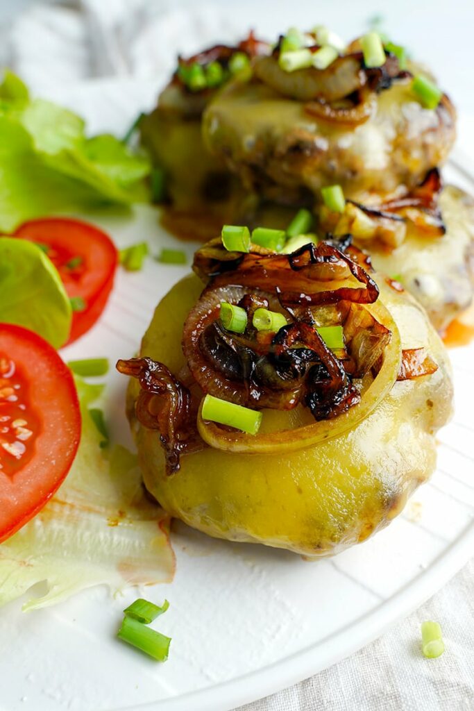 Grilled onion and cheese burgers on a plate with tomatoes and lettuce