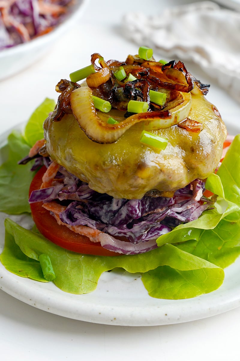 Grilled Onion Cheddar Burger patties on a bed of coleslaw, tomato and lettuce